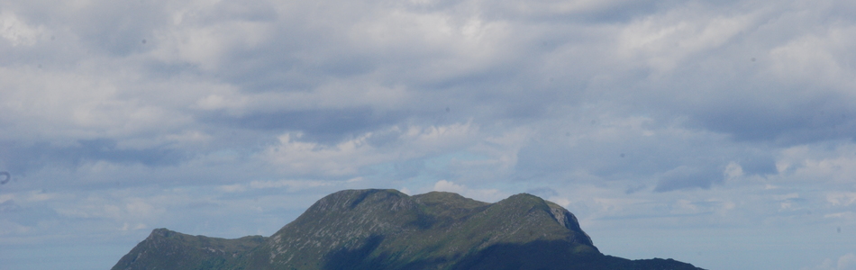 Foto av tindepreget ås- og fjellandskap med hei under skoggrensen